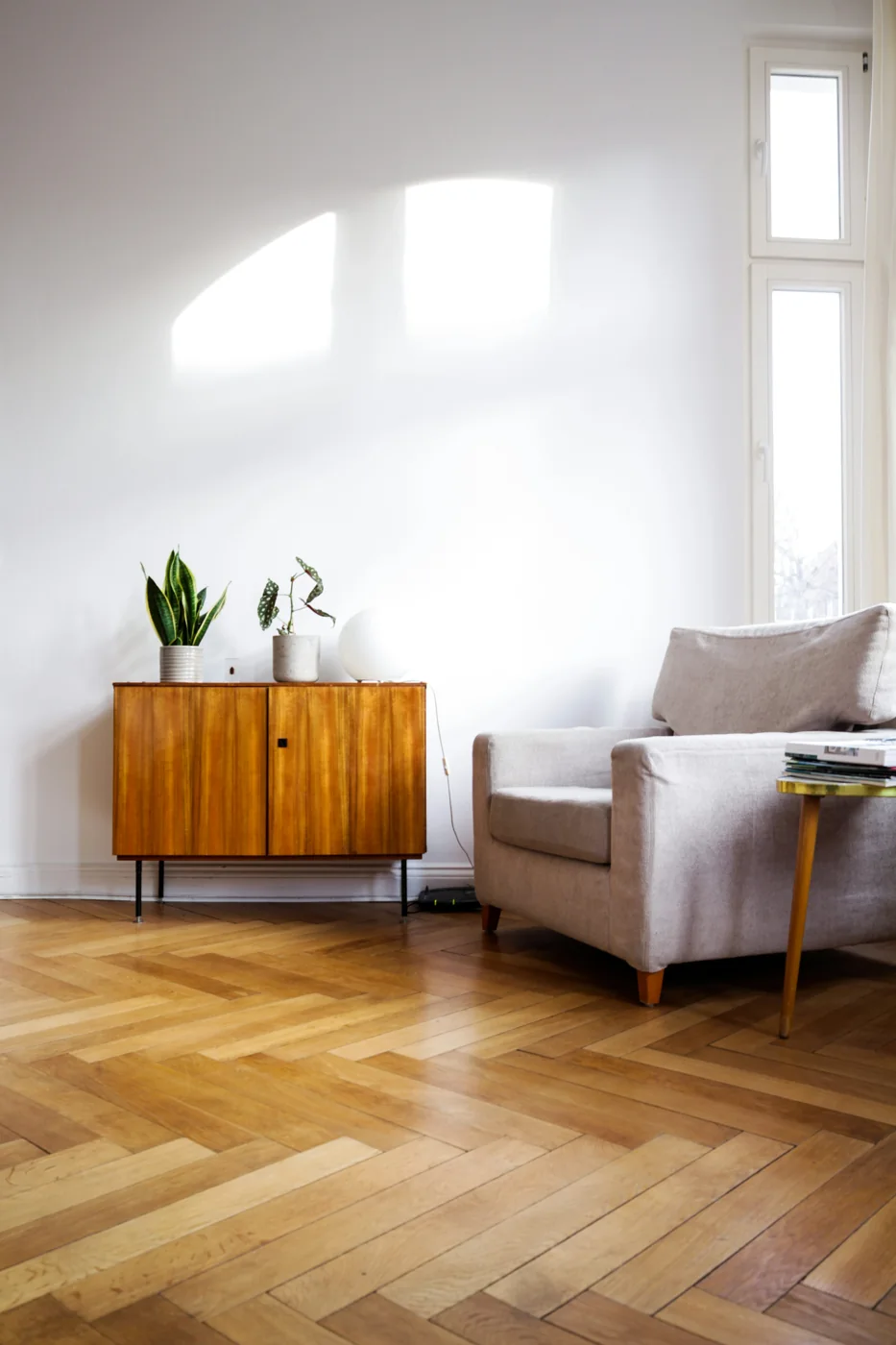 Illustrative stock photograph of a pale armchair, wooden sideboard and sunlit parquet flooring